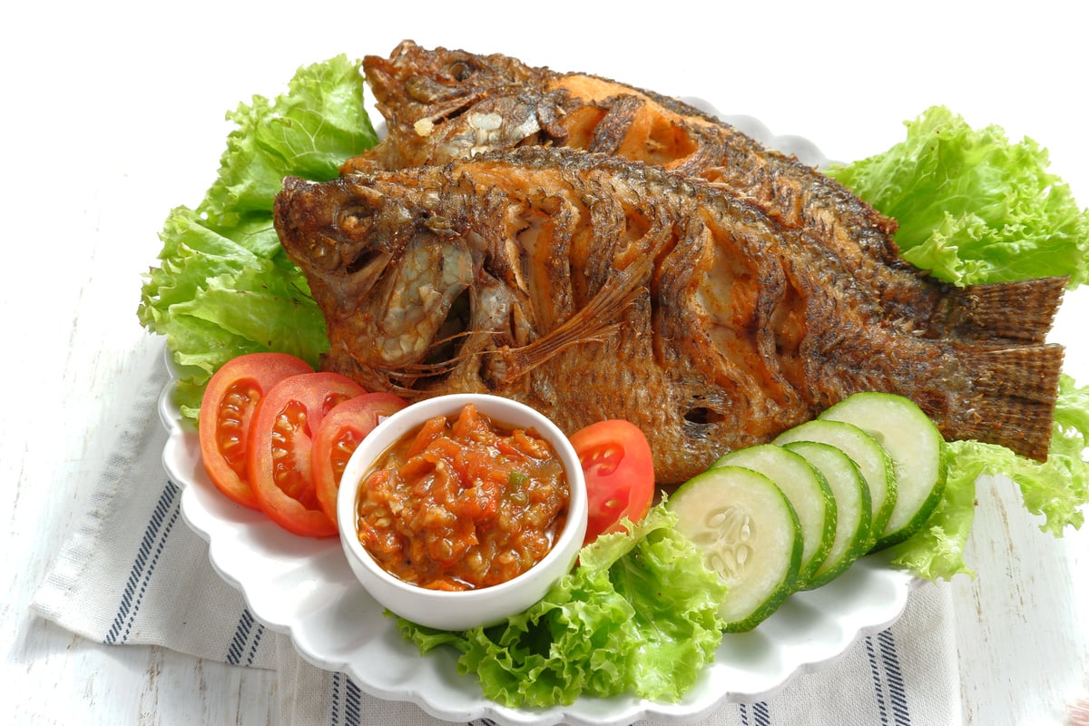 Fried Tilapia or Ikan Nila Goreng. Served on white plate with lettuce,cucumber and tomato